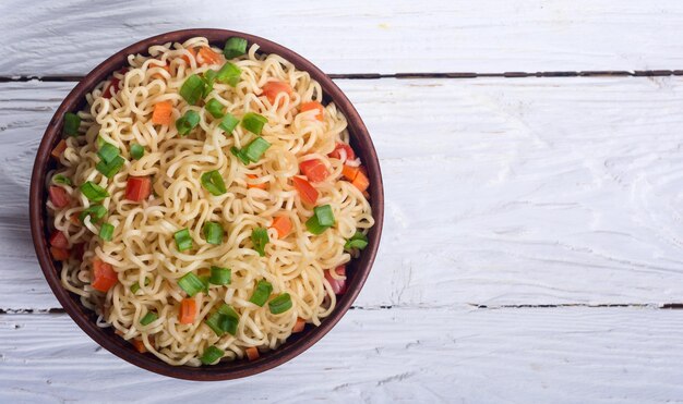 Instant noodles in bowl with carrot tomatoes and onion
