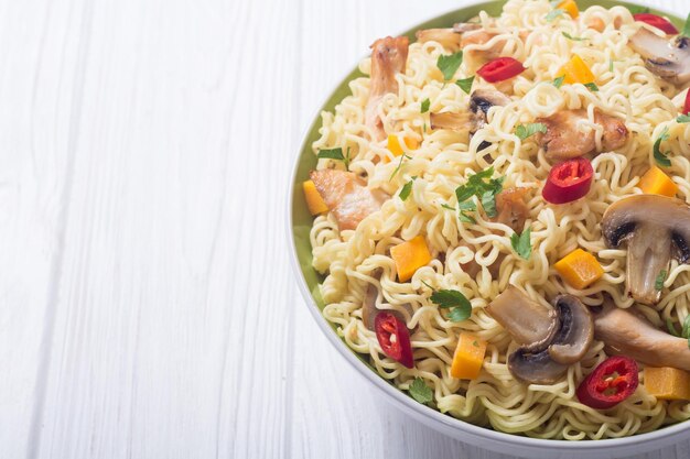 Instant noodles in bowl with chili peppers mushrooms chicken and carrots