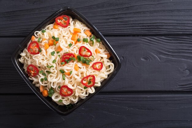 Instant noodles in bowl with chili peppers onion and carrots