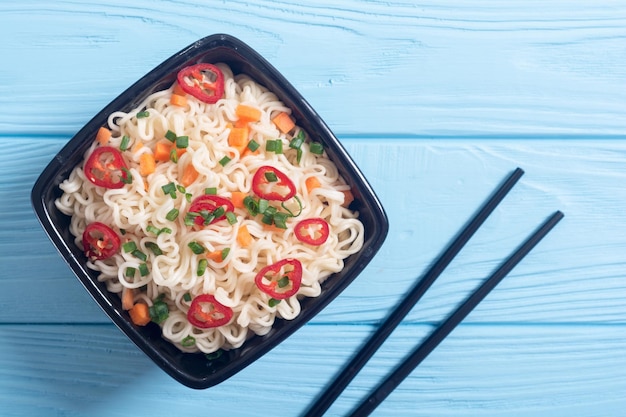 Instant noodles in bowl with chili peppers onion and carrots