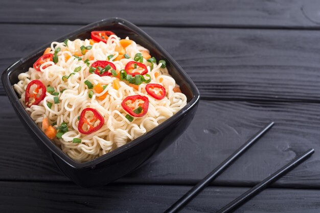 Instant noodles in bowl with chili peppers onion and carrots