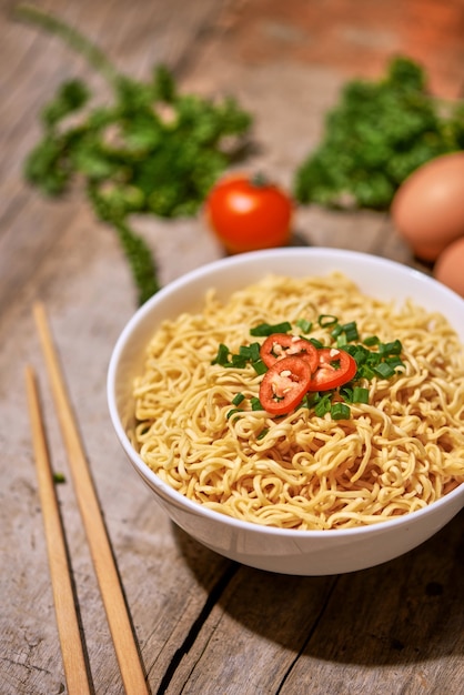 Instant noodles in bowl with vegetable on wooden table.