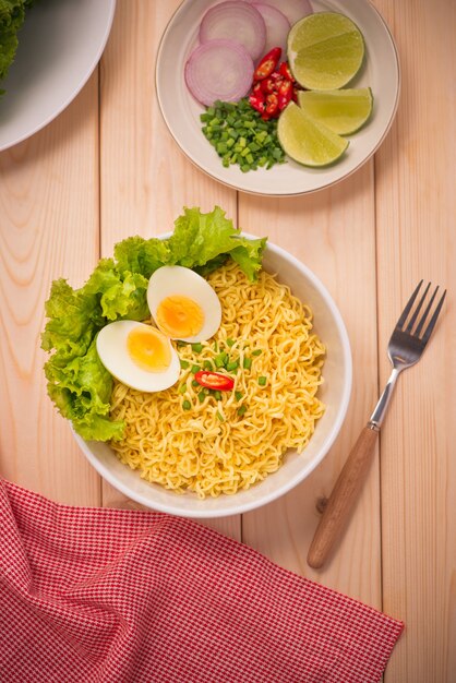 Instant noodles in bowl with vegetables and  boiled egg on wood background