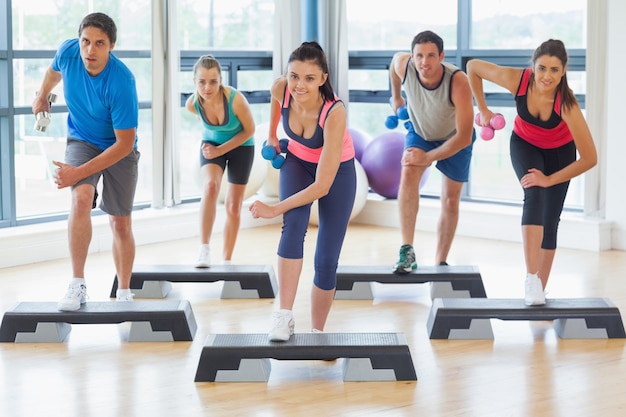 Instructeur met fitness klasse uitvoeren van stap-aerobics-oefening met halters