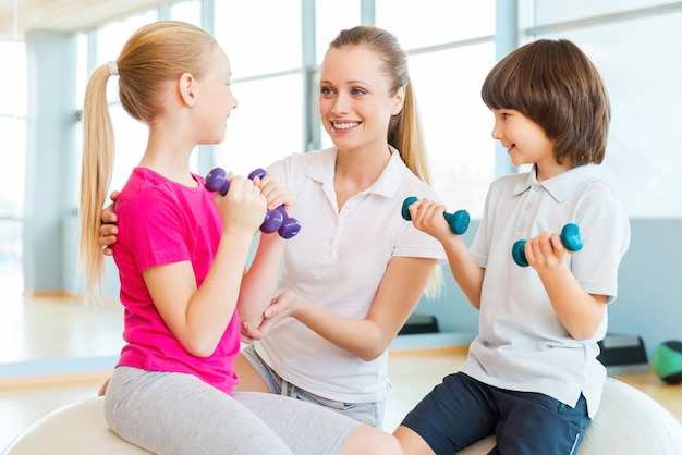 Instructeur met kinderen. Vrolijke instructeur die kinderen helpt met sporten in de gezondheidsclub