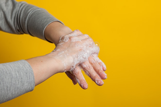 Instruction to carefully wash your hands and nails . Women's hands in a soap solution on a bright background