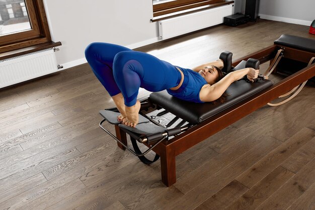 The instructor does exercises on the reformer a beautiful girl trains on the modern reformer simulator to work out deep muscles the modernized reformer equipment for Pilates and yoga