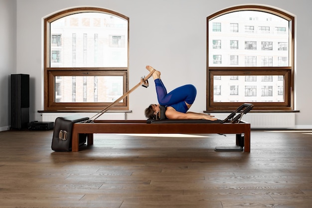The instructor does exercises on the reformer a beautiful girl trains on the modern reformer simulator to work out deep muscles the modernized reformer equipment for Pilates and yoga