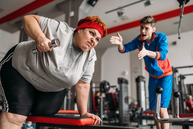 Istruttore costringe la donna grassa a fare esercizio con i manubri in palestra.