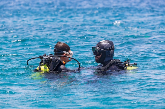 Istruttore che dà lezioni di immersione a un bambino istruttore di immersione che insegna a un bambino ad immergersi corso per sub due subacquei nel mar rosso poco profondo subacquei vestiti con tuta da sub aqualung