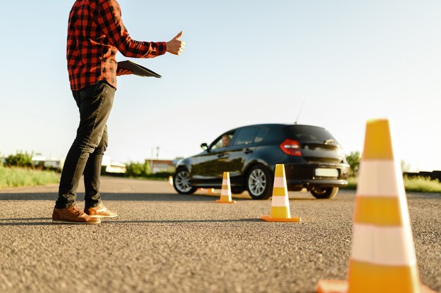 Photo instructor helps female student to drives between cones, lesson in driving school.