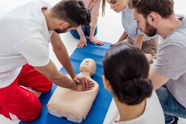 Photo instructor performing cpr on dummy during first aid training with group of people