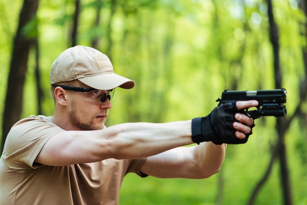 Инструктор с пистолетом в лесу ведет цель и позирует на камеру