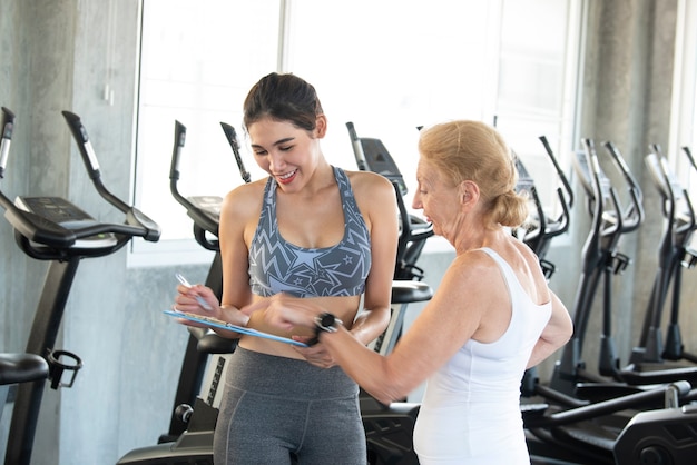 Instructor with senior woman in rehabilitation center. Personal trainer showing something on document clipboard.