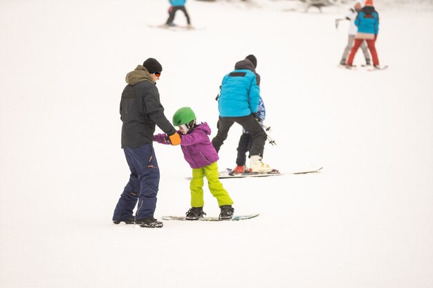 Instructors teach a child on a snow slope to snowboard