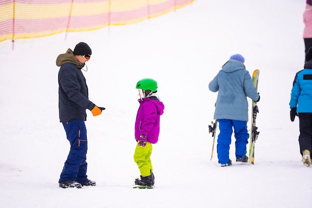 Instructors teach a child on a snow slope to snowboard