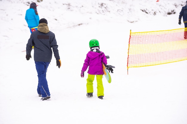 Instructors teach a child on a snow slope to snowboard