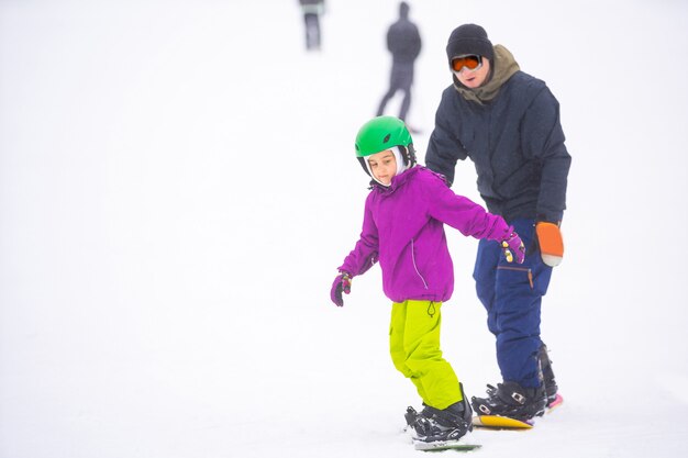 インストラクターは、スノースロープで子供にスノーボードを教える