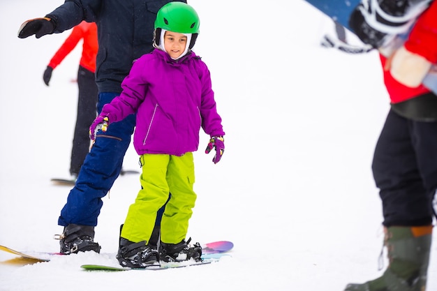 Instructors teach a child on a snow slope to snowboard