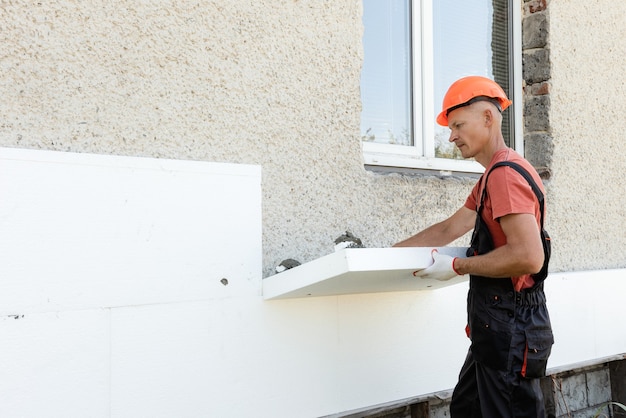 Isolamento della casa con polyfoam. il lavoratore sta installando un pannello di polistirolo sulla facciata.