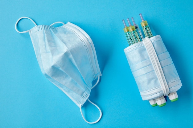 Insulin syringe pens wrapped with medical masks on a blue background Risk of viral complications in diabetic patients Protection from covid infection Top view Flat lay