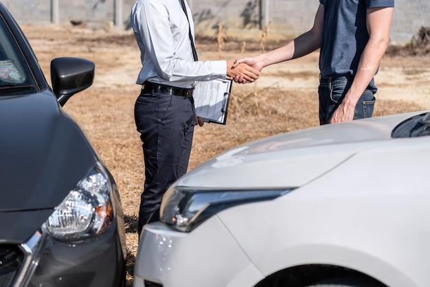 Страховой агент и клиент пожимают друг другу руки после согласования страховой претензии, оценивают осмотр автокатастрофы, проверяют и подписывают процесс подачи заявления после аварии