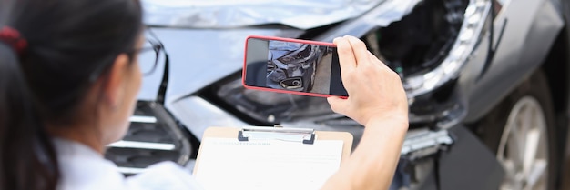 Insurance agent takes pictures of damage to car after accident on smartphone filling out