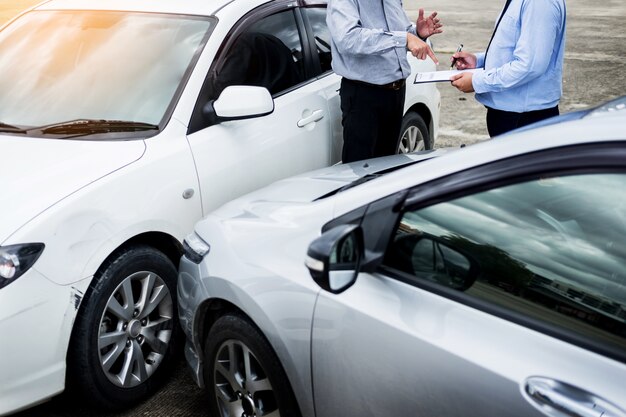 Photo insurance agent writing on clipboard while examining car after accident