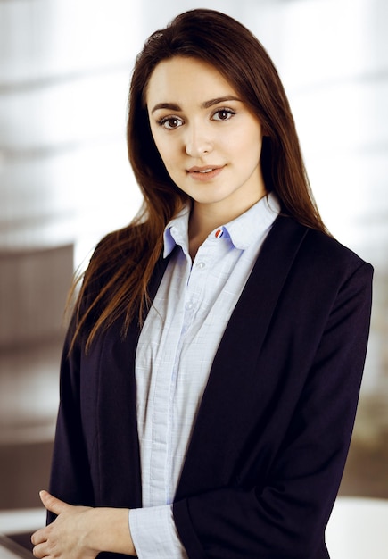 Foto intelligente giovane donna d'affari in una giacca blu è in piedi al suo posto di lavoro. ritratto di uno specialista in un ufficio moderno.