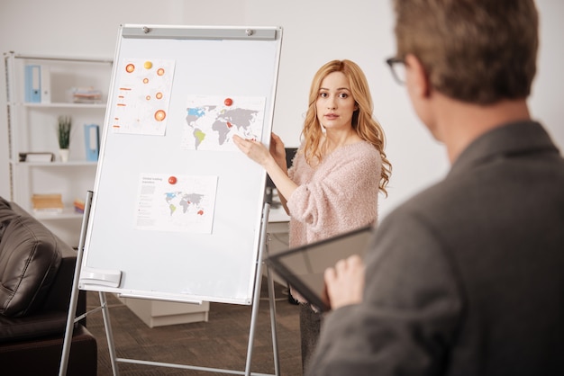 Foto intelligente, verlegen professionele officemanager die voor het whiteboard op kantoor staat en het project tijdens het werken voor de baas vertegenwoordigt