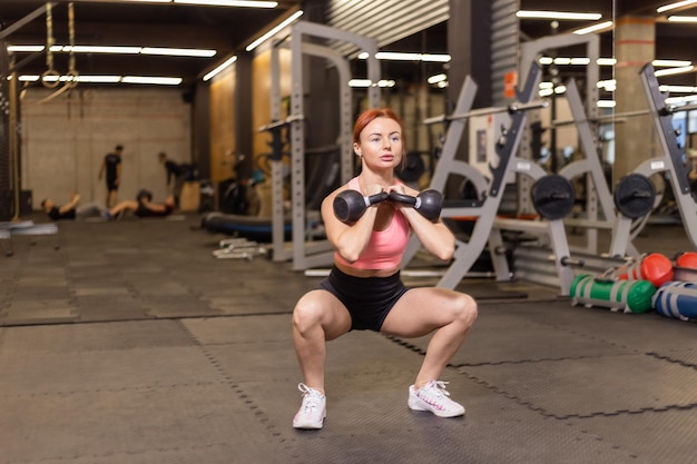 Intensieve training roodharige vrouw met kettlebells in haar hand in moderne sportschool