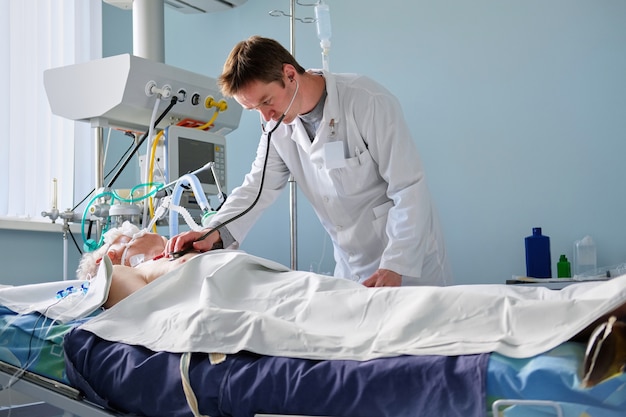 Intensive care caucasian doctor examines intubated critical stance patient in intensive care department