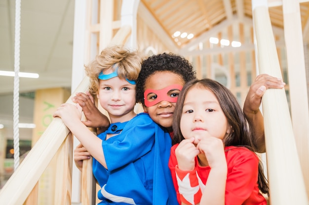 Piccoli amici interculturali in costumi seduti sulle scale davanti alla telecamera mentre giocano insieme nella stanza dei bambini