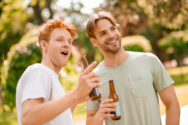 Interessant hier. Glimlachende vrolijke jongens in lichte t-shirts met flessen die iets interessants zien dat aandachtig observeert in het park op mooie dag