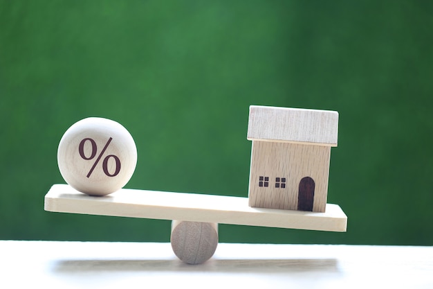 Interest rate up and Banking concept, Model house with Floating rate on wood scale seesaw on natural green background, Mortgage rates