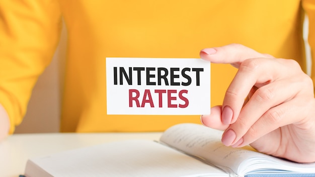 Interest rates is written on a white business card. A woman's hand holds a white paper card. 