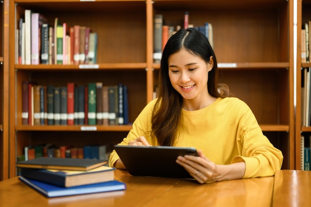 Interested asian female student using digital tablet doing class assignment in library Education learning and people concept