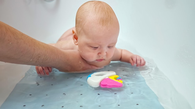 Interested baby girl plays with father and toy in water