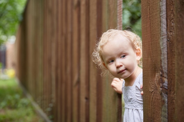 Interested child looks out through a hole in a brown wooden fence.