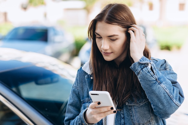 Ragazza interessata che raddrizza i capelli, guardando qualcosa su uno smartphone per strada.