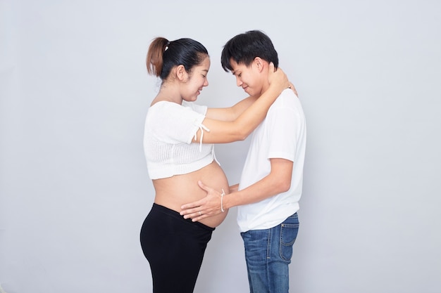 Interessante coppia asiatica, madre incinta felice e padre isolato su superficie bianca, giornata internazionale della famiglia