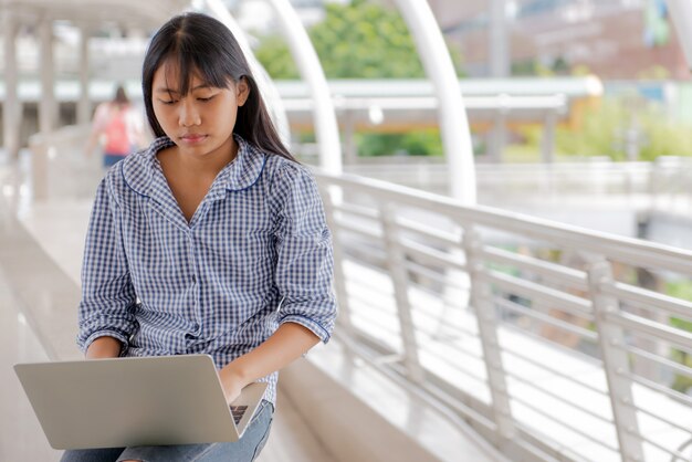 Interessanti ragazze asiatiche digitando, chiacchierando, seduti, chiacchierando, rispondendo usando un laptop devic