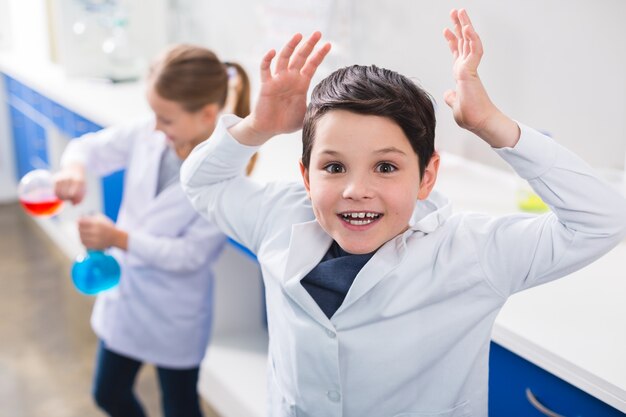 Interesting chemistry. Happy nice smart boy holding his hands up and looking at you while conducting a chemical experiment