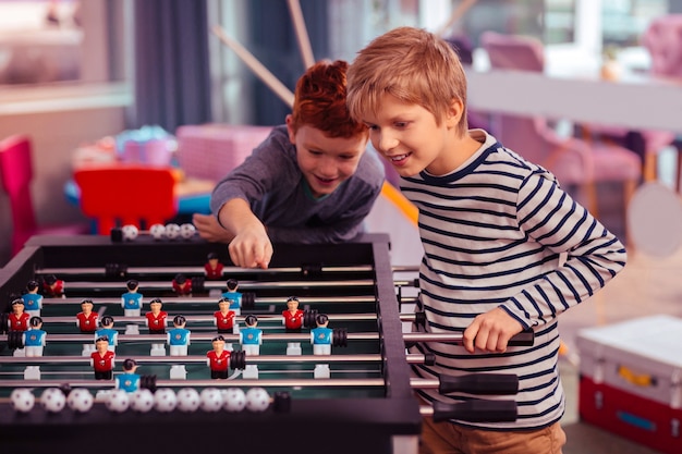 Interesting game. Cheerful blonde boy standing in semi position and looking at kicker football