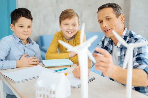 Интересная информация. приятный жизнерадостный отец показывает на стоящие на его столе модели ветряных турбин и обсуждает их конструкцию со своими любопытными сыновьями.