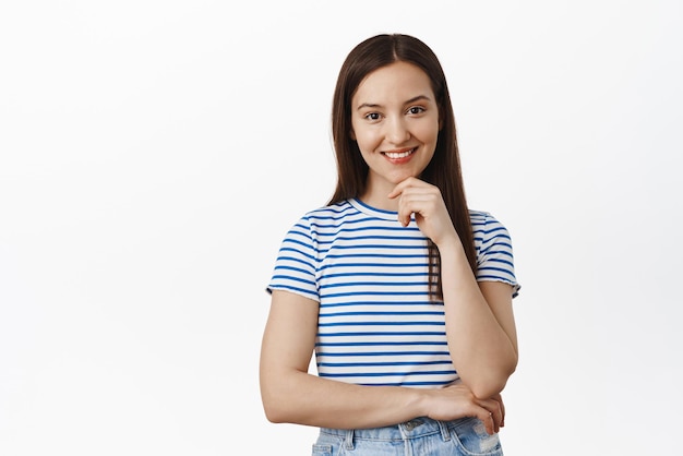 Interesting Smiling thoughtful girl listening intrigued touch chin and thinking standing thoughtful has an idea posing in tshirt against white background