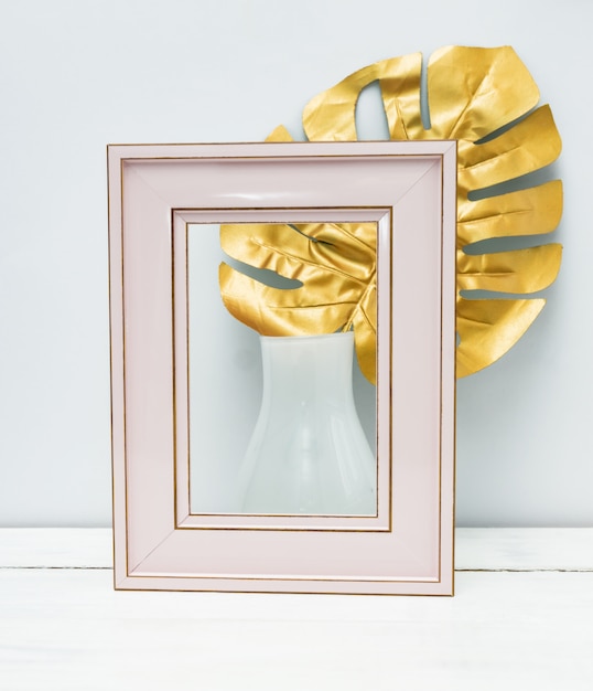 Interieur ontwerp. Leeg roze photoframe en monsterablad in witte vaas op witte muurachtergrond.