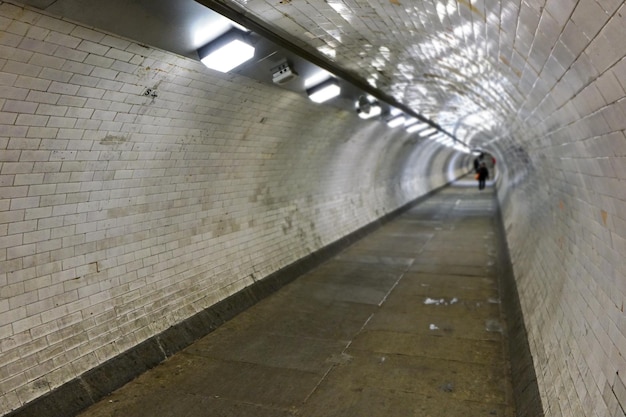 Interieur van de voettunnel van Greenwich die beide zijden van Londen verbindt onder de rivier de Theems, verlicht door neonlichten, groothoekfoto met wazige voetgangers op afstand.