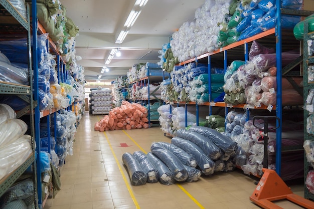 Interieur van een industrieel magazijn met veel planken met kleurrijke stoffenrollen erop De arbeider tilt de rolstof op en controleert de hoeveelheid