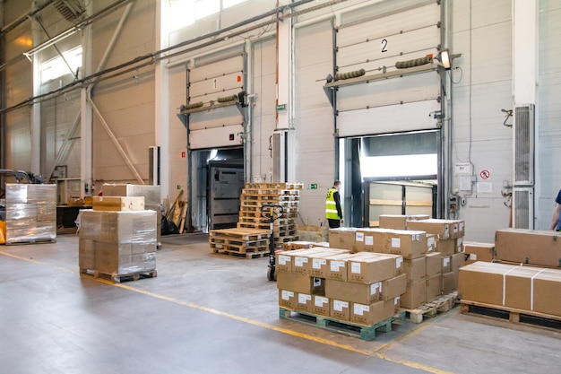 Interieur van een moderne magazijnopslag van een winkel met pallettruck in de buurt van planken en laadhellingen Magazijnmedewerker in uniform aan het werk op vorkheftruck